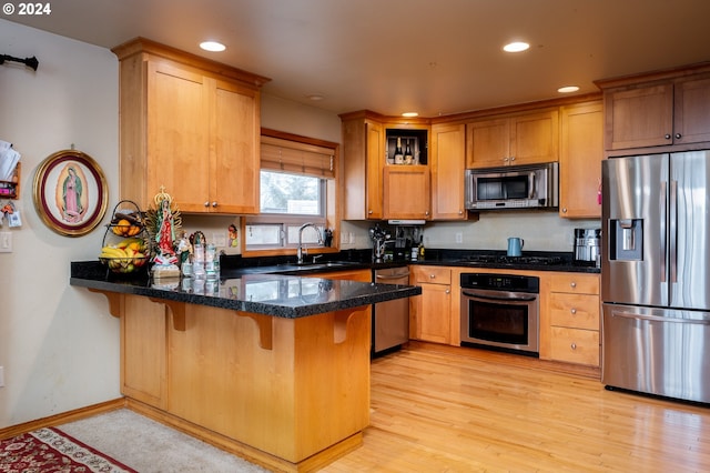 kitchen with sink, dark stone countertops, light wood-type flooring, kitchen peninsula, and stainless steel appliances