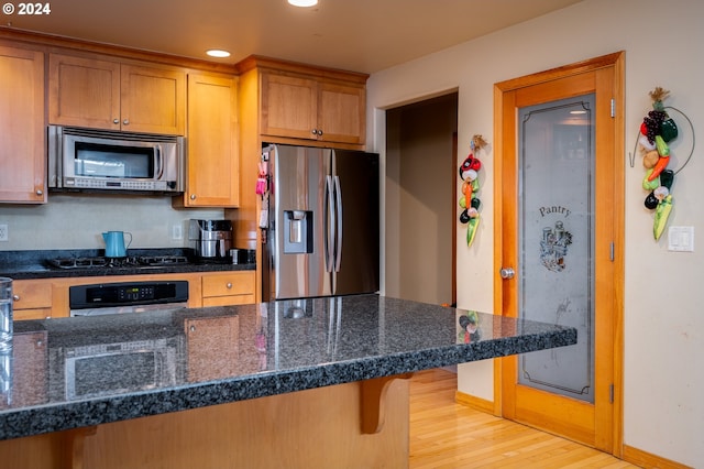 kitchen featuring a kitchen bar, light wood-type flooring, stainless steel appliances, and dark stone counters