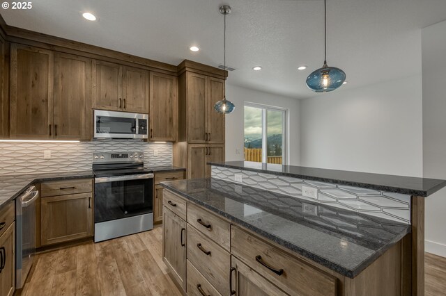 kitchen featuring a kitchen island, appliances with stainless steel finishes, dark stone countertops, light hardwood / wood-style floors, and decorative light fixtures