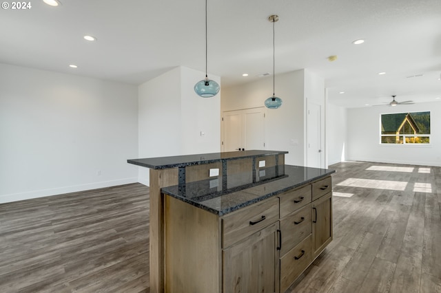 kitchen with dark hardwood / wood-style floors, hanging light fixtures, dark stone countertops, a center island, and ceiling fan