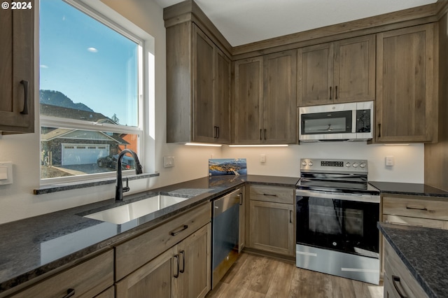 kitchen with appliances with stainless steel finishes, light hardwood / wood-style floors, sink, and dark stone countertops