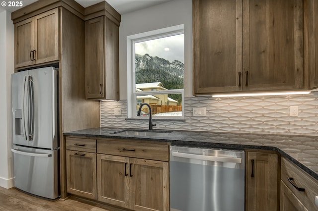 kitchen with sink, light hardwood / wood-style flooring, dark stone countertops, appliances with stainless steel finishes, and decorative backsplash