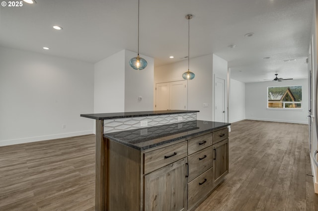 kitchen featuring a breakfast bar area, wood-type flooring, hanging light fixtures, ceiling fan, and dark stone counters