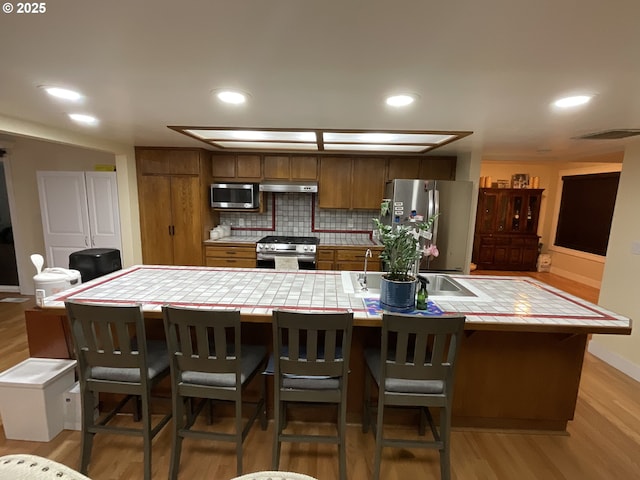 kitchen with light hardwood / wood-style flooring, appliances with stainless steel finishes, tasteful backsplash, tile counters, and a breakfast bar area