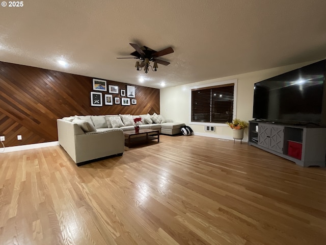 unfurnished living room featuring hardwood / wood-style floors, ceiling fan, a textured ceiling, and wooden walls