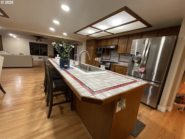 kitchen featuring sink, stainless steel appliances, tile counters, and an island with sink