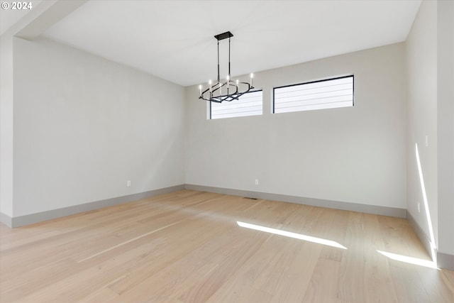 unfurnished room with a notable chandelier, light wood-style flooring, and baseboards