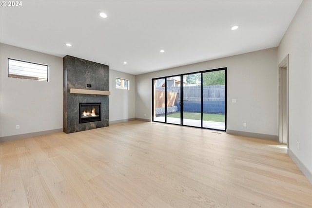 unfurnished living room with a tiled fireplace, recessed lighting, baseboards, and light wood-style floors