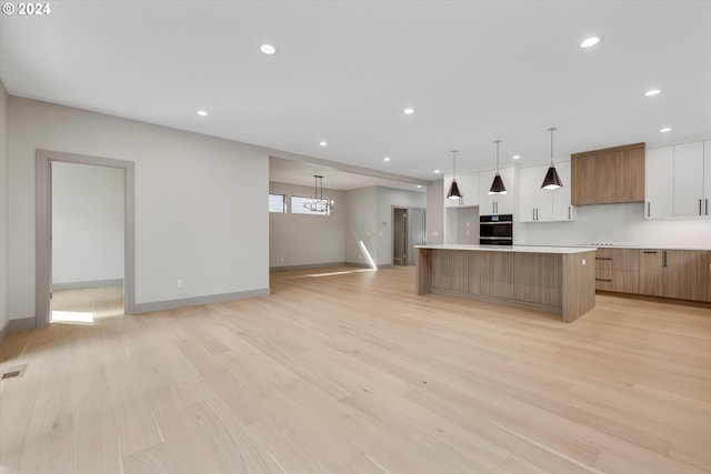 kitchen with black oven, a large island, modern cabinets, and light wood-style flooring