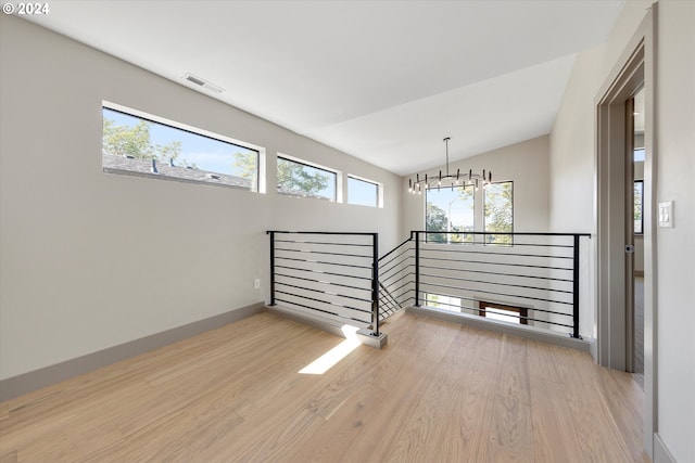 empty room with visible vents, a notable chandelier, wood finished floors, and vaulted ceiling