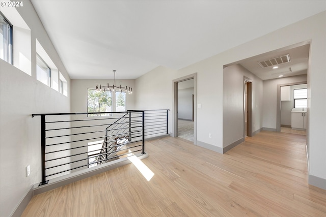 unfurnished room with an inviting chandelier, light wood-style floors, visible vents, and baseboards