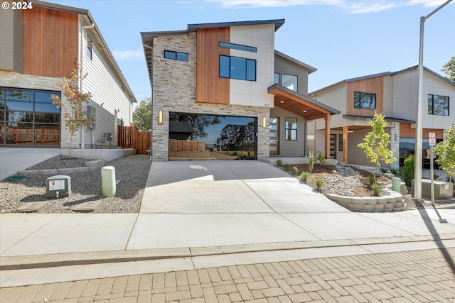 contemporary home with fence, stone siding, and driveway