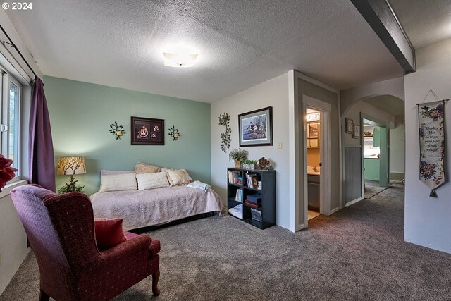 bedroom featuring ensuite bathroom, a textured ceiling, and dark colored carpet