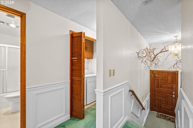 corridor featuring a notable chandelier, washer / dryer, light colored carpet, and a textured ceiling