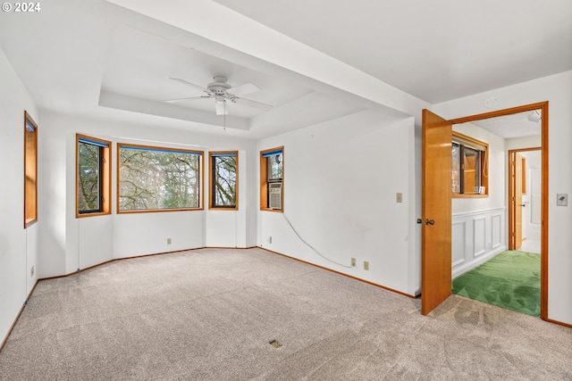 empty room with light carpet, a raised ceiling, and ceiling fan