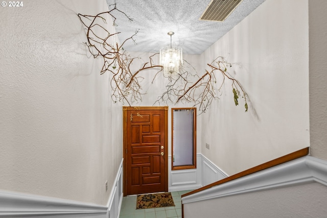 tiled foyer with a textured ceiling and a notable chandelier