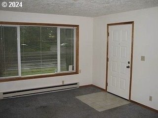 carpeted foyer entrance featuring baseboard heating and a textured ceiling