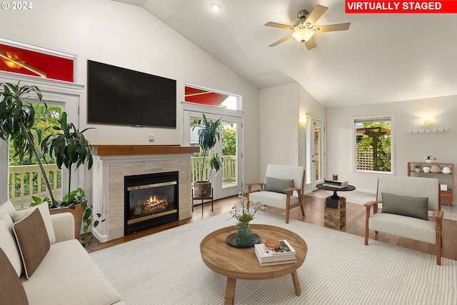 living room with ceiling fan, a tiled fireplace, a healthy amount of sunlight, and vaulted ceiling