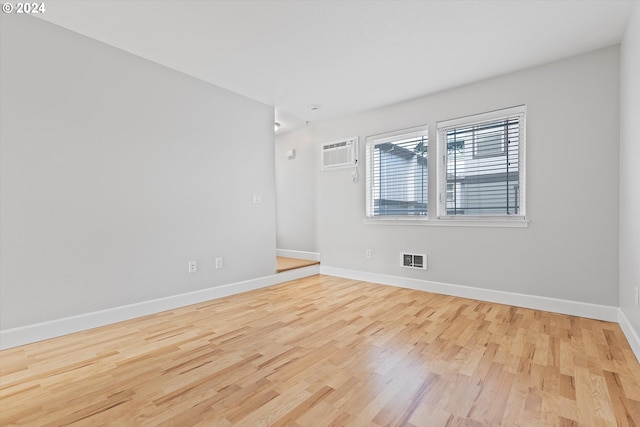 empty room with an AC wall unit and light wood-type flooring