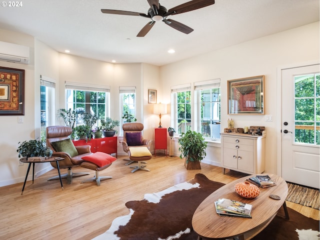 living room featuring ceiling fan, a healthy amount of sunlight, an AC wall unit, and light hardwood / wood-style flooring