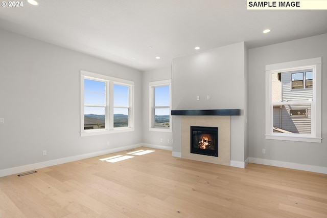 unfurnished living room with light hardwood / wood-style floors, a tile fireplace, and a wealth of natural light