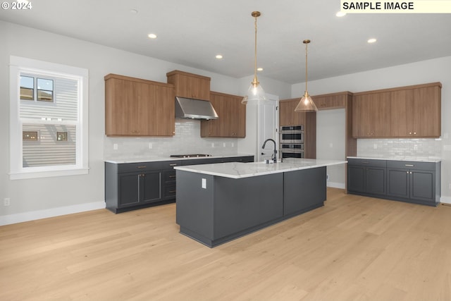 kitchen featuring a center island with sink, light wood-type flooring, pendant lighting, stainless steel double oven, and black electric stovetop