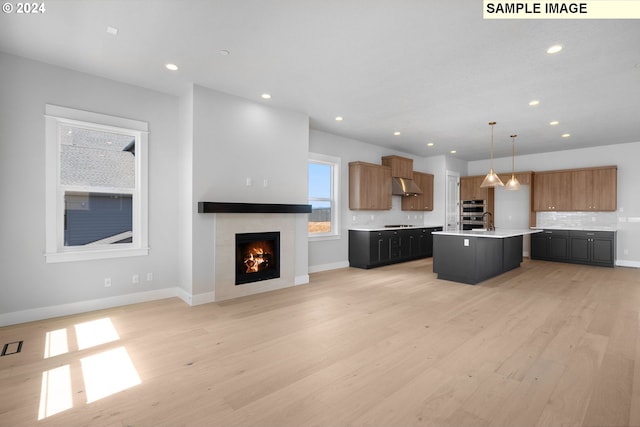 kitchen with a kitchen island with sink, ventilation hood, light hardwood / wood-style floors, decorative light fixtures, and decorative backsplash