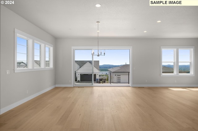 unfurnished living room featuring a notable chandelier, a mountain view, a textured ceiling, and light wood-type flooring