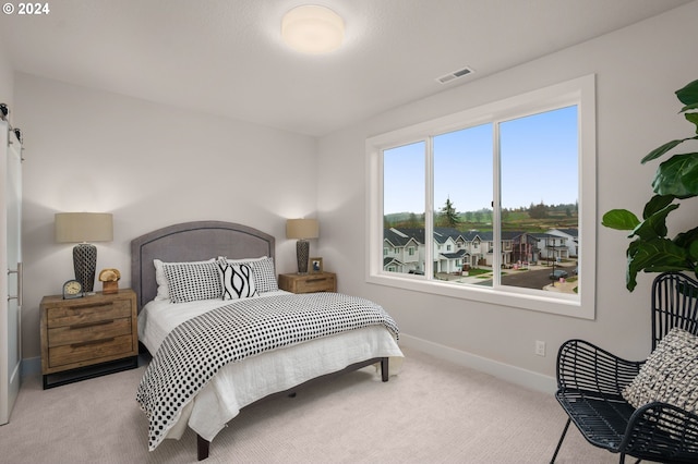 bedroom with light carpet, baseboards, visible vents, and a barn door