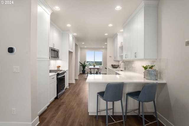 kitchen with kitchen peninsula, appliances with stainless steel finishes, dark wood-type flooring, white cabinetry, and a breakfast bar area