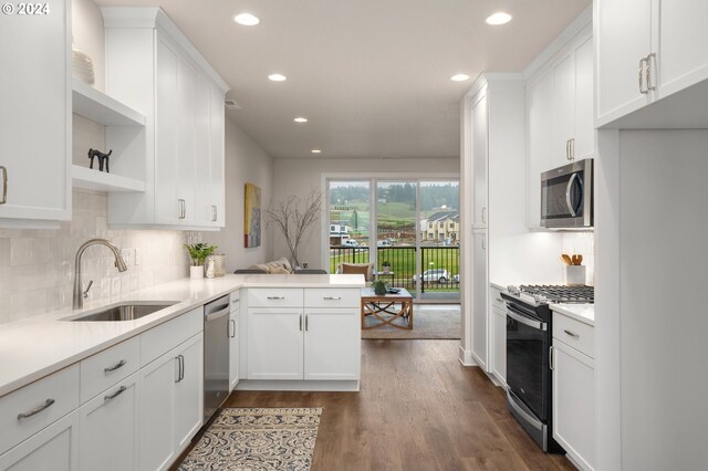 kitchen with a peninsula, stainless steel appliances, light countertops, white cabinetry, and a sink