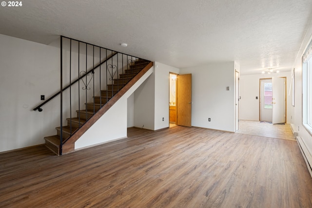 unfurnished living room with hardwood / wood-style floors, a textured ceiling, and baseboard heating