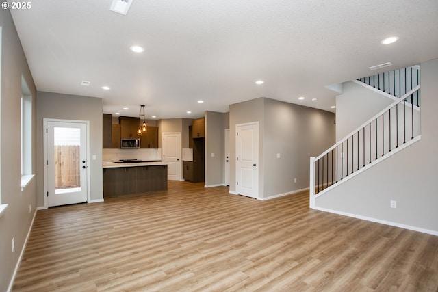 unfurnished living room with recessed lighting, baseboards, stairway, and light wood finished floors