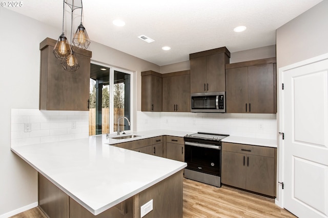 kitchen with stainless steel appliances, a peninsula, a sink, and light countertops