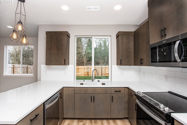 kitchen with stainless steel appliances, light countertops, visible vents, a sink, and a peninsula