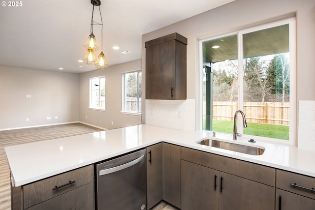 kitchen with a peninsula, stainless steel dishwasher, a sink, and light countertops