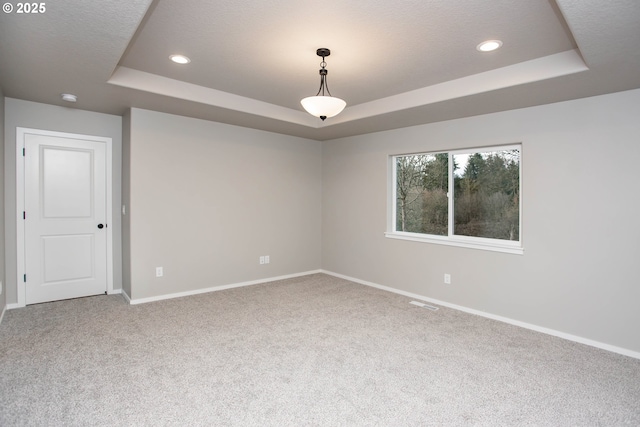 carpeted empty room featuring a tray ceiling, visible vents, baseboards, and recessed lighting