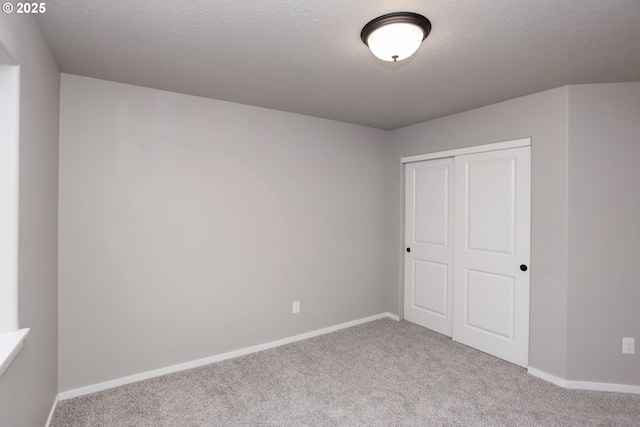 unfurnished bedroom with a textured ceiling, a closet, baseboards, and carpet flooring