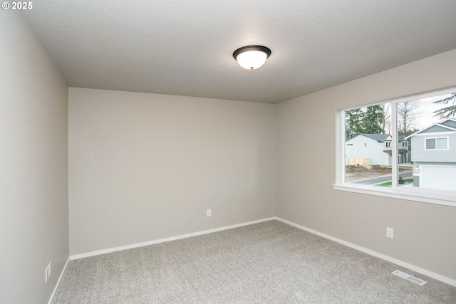 empty room with carpet floors, visible vents, a textured ceiling, and baseboards