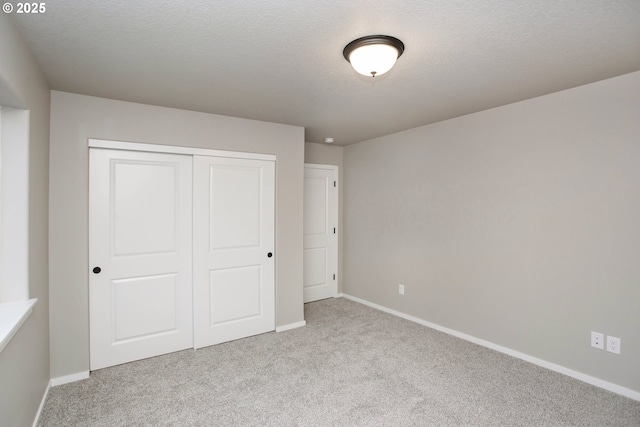 unfurnished bedroom with a textured ceiling, a closet, carpet flooring, and baseboards