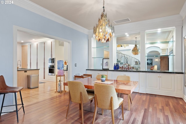 dining room with light wood-type flooring, crown molding, a notable chandelier, and sink