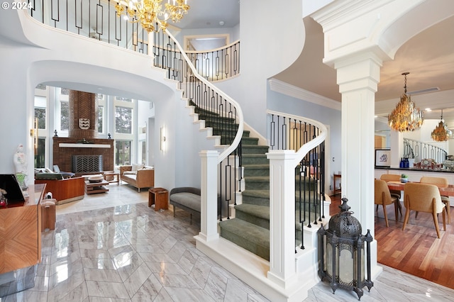 entrance foyer with crown molding, a chandelier, a high ceiling, and a brick fireplace