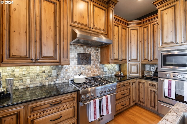 kitchen featuring dark stone countertops, backsplash, appliances with stainless steel finishes, and light hardwood / wood-style flooring