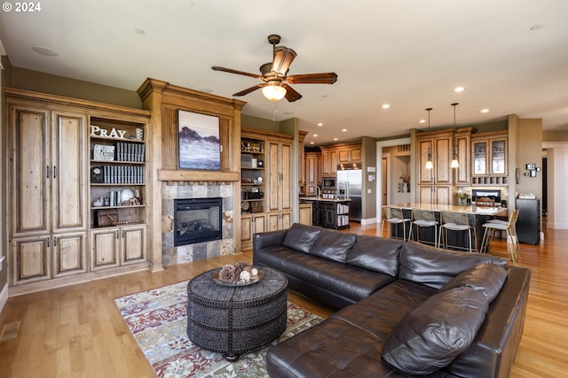 living room with ceiling fan, light hardwood / wood-style floors, and a tiled fireplace