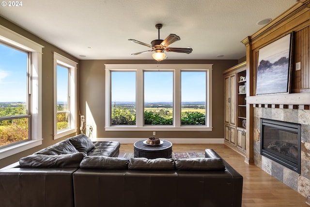 living room featuring a tiled fireplace, a wealth of natural light, ceiling fan, and light hardwood / wood-style floors