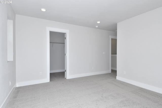 unfurnished bedroom featuring a walk in closet, a closet, and light colored carpet