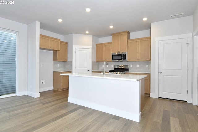 kitchen with a center island with sink, light wood-type flooring, backsplash, and appliances with stainless steel finishes