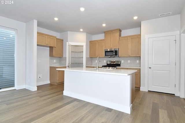 kitchen featuring backsplash, light wood-type flooring, a kitchen island with sink, and appliances with stainless steel finishes