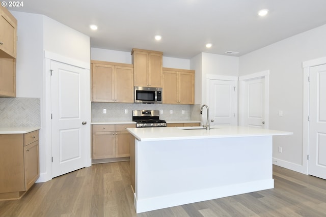 kitchen featuring light brown cabinetry, light wood-type flooring, stainless steel appliances, a kitchen island with sink, and sink