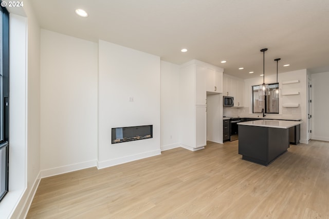 kitchen with appliances with stainless steel finishes, white cabinetry, light hardwood / wood-style floors, decorative light fixtures, and a center island